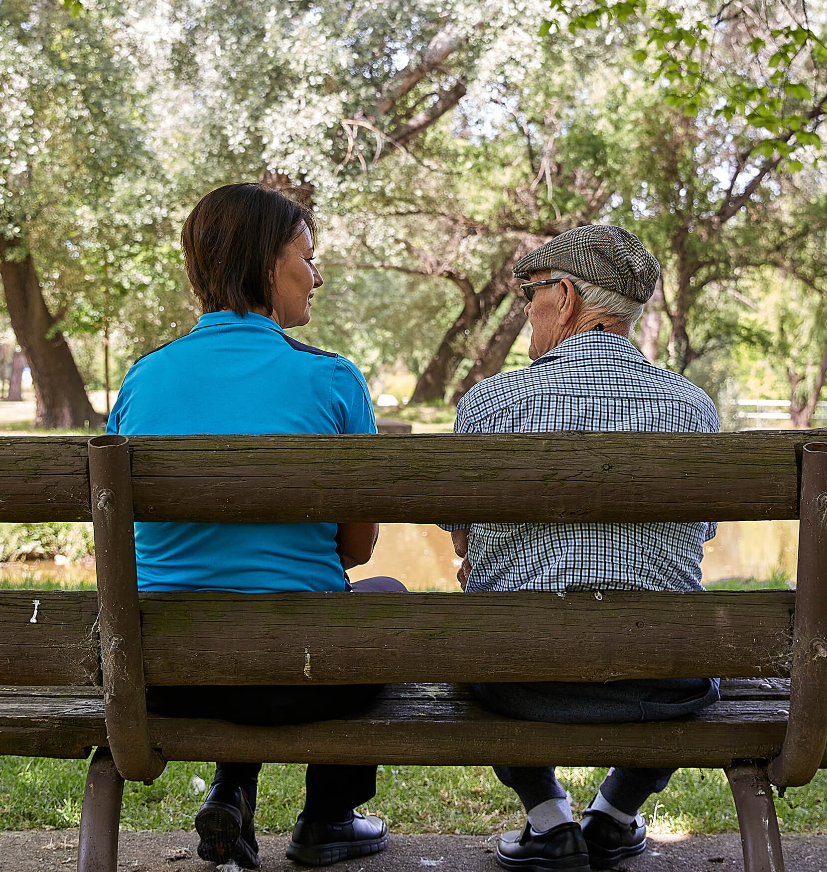 A younger woman and a senior man sitting on a park bench in conversation 